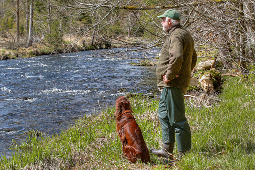 A hiker and his Irish Setter stand by the scenic Regen River. The gentle murmur of the water and the breathtaking landscape made the two pause and enjoy the beauty of the moment.