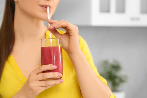 istock Woman drinking delicious smoothie in kitchen, closeup. Space for text 1490933510