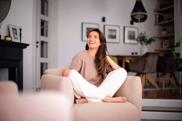 Brunette haired woman cheerful smiling and relaxing in an armchair at home stock photo