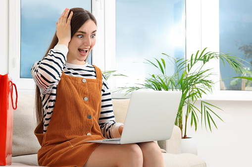 Special Promotion. Emotional woman looking at laptop on sofa indoors