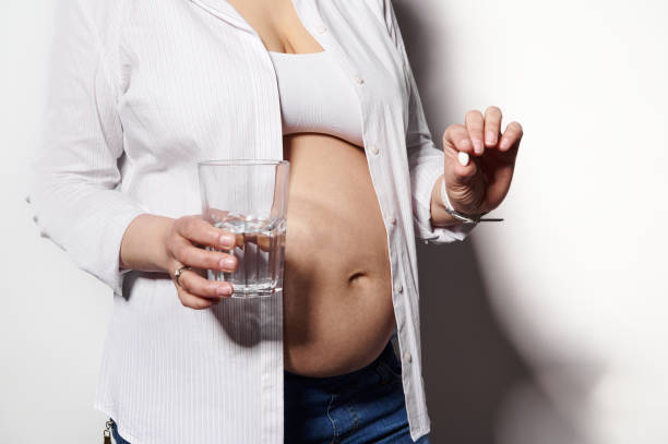 임신 중에 복용할 비타민과 미네랄이 담긴 물 한 잔과 의료용 알약을 들고 있는 클로즈업 임산부 - 엽산 뉴스 사진 이미지