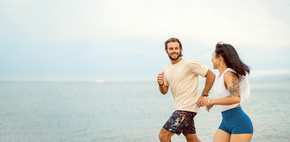 Cheerful young multi-ethnic couple running on the sandy sea beach in summer sport clothing