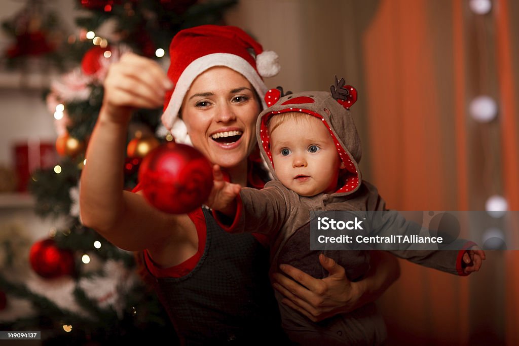 Happy mother showing Christmas ball  to baby Happy mother showing Christmas ball  to baby near Christmas tree Baby - Human Age Stock Photo