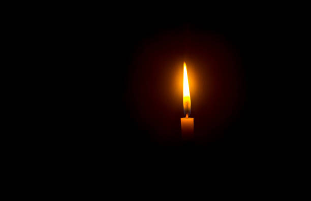 istock A single burning candle flame or light glowing on an orange candle on black or dark background on table in church for Christmas, funeral or memorial service with copy space 1490942157