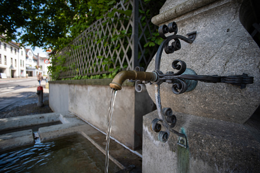 Old stone and metal public drinking water fountain in a city in Switzerland, Europe. Daytime, wide angle, no peop.