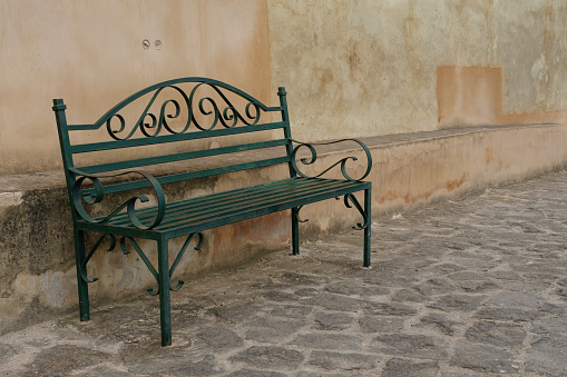 Green metal bench on a natural stone floor in front of a weathered wall.