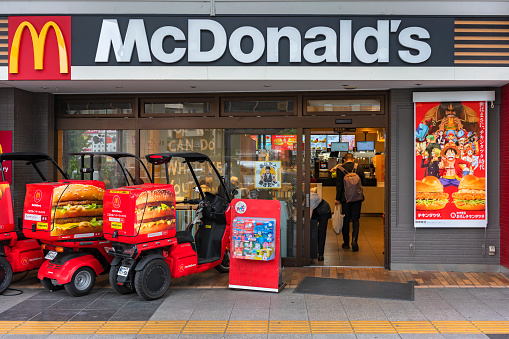 tokyo, japan - april 11 2023: Japanese Honda Gyro Canopy three-wheeler motorcycles used for McDelivery parked at McDonald's with an advertising poster featuring One Piece anime and manga characters.