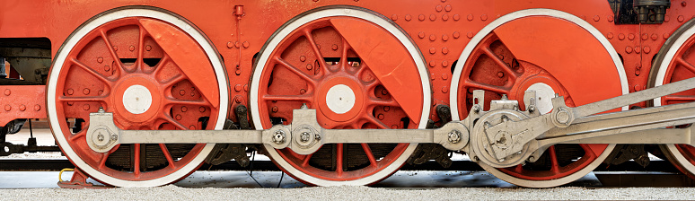 Big red wheels, flywheels, connecting rods and other machinery of an old steam locomotive.