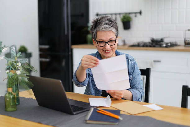 happy mature woman in glasses opens mail documentation at the table. - news of the world imagens e fotografias de stock