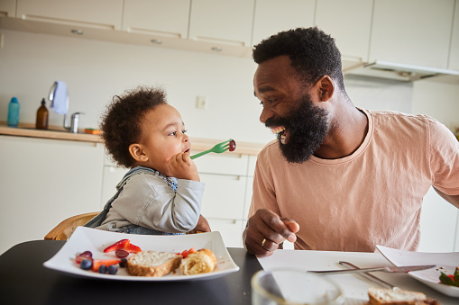 istock Little boy feeding his smiling dad during a family breakfast in the morning 1490953538