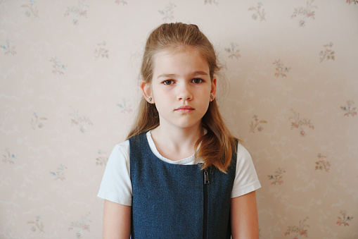 Portrait of a sad teenage girl with long blonde hair in a gray sundress and a white t-shirt. The concept of school and online learning. Psychological assistance for children.