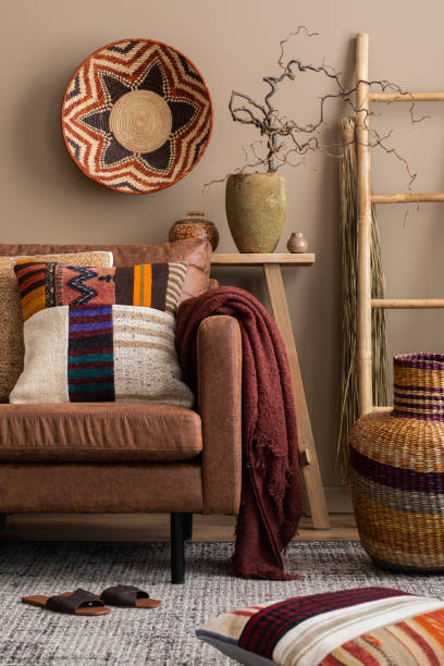 istock Creative composition of living room interior with brown sofa, colorful pillows, patterned baskets, ladder slippers, vase with branch and personal accessories. Home decor. Template. 1490957537