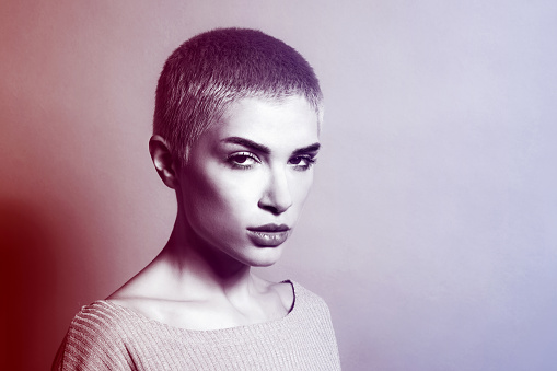 Portrait of serious young female model with short hair looking at camera against studio background