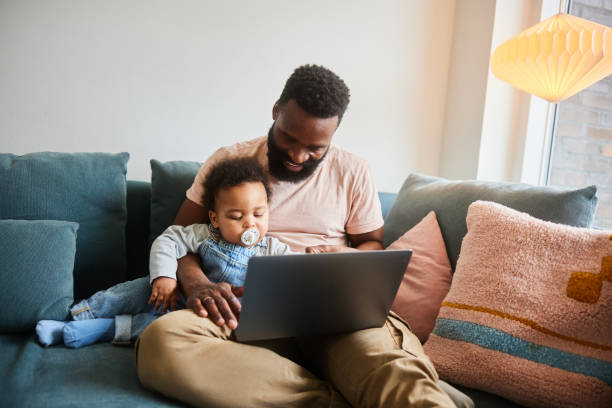 istock Dad working on a laptop while sitting with his baby boy on a sofa 1490959920