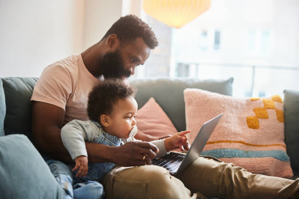 tata pracujący na laptopie siedzący z małym synkiem na kanapie - family sofa men sitting zdjęcia i obrazy z banku zdjęć