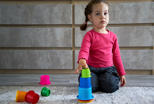 Cute child playing colorful pyramid. Little girl playing with pyramid toy on a floor at home