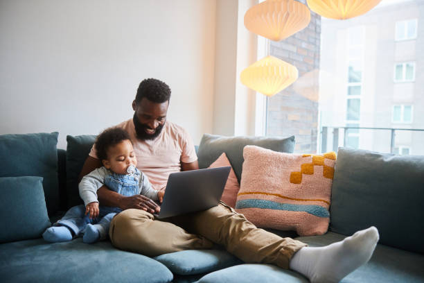 istock Dad sitting with his baby boy on a sofa and working on a laptop 1490962830