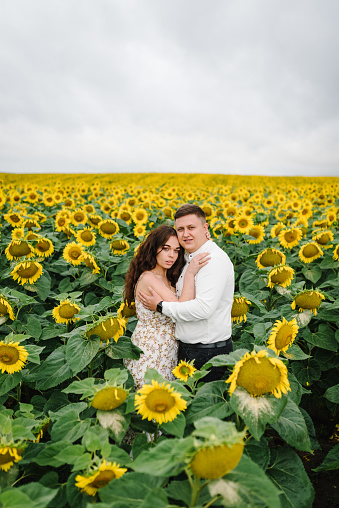 Man and woman hugging, enjoying glade, embrace in nature. Couple hugs in sunflowers field. Honeymoon trip. Weekend vacation holidays concept. Love story on summer day. Selective focus. Romantic moment