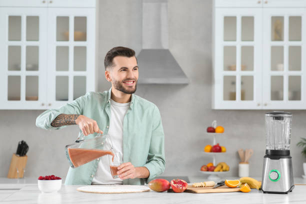 istock Handsome man pouring tasty smoothie into glass at white marble table in kitchen. Space for text 1490965292