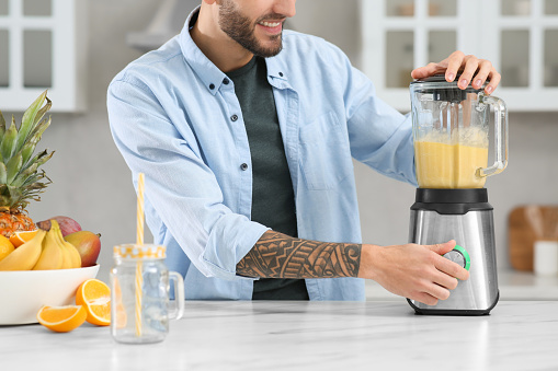 Man preparing ingredients for tasty smoothie at white marble table in kitchen, closeup