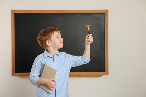 Cute little boy ringing school bell in classroom