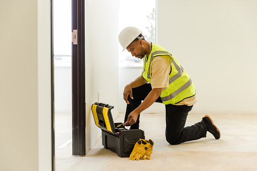 The male electrician kneels down to look for tools to fix issues at the job site before the inspector arrives.