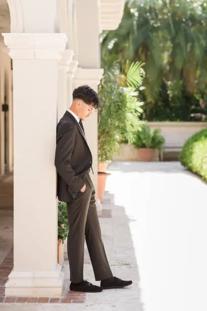 Photo of 2023 High-School Senior Young Man Well-Dressed in a Black Suit, White Dress Shirt, Black Tie & Black Suede Shoes, An18-Year-Old Cuban-American with Brown Hair & Brown Eyes Looking Fresh & Sharp in a Suit & Tie in a Classy Location in Palm Beach, Florida