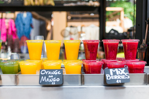 Close up color image depicting freshly made fruit juices and smoothies on display in a row and for sale at a food and drink market in London, UK. Selective focus on the plastic cups containing the fresh smoothies. Room for copy space.
