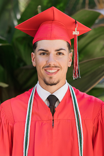 2023 High-School Senior Young Man in a Red Graduation Cap & Gown With Three Honors Tassels, A Well-Dressed 18-Year-Old Cuban-American with Brown Hair & Brown Eyes Looking Fresh & Sharp in a Suit & Tie in a Classy Location in Palm Beach, Florida