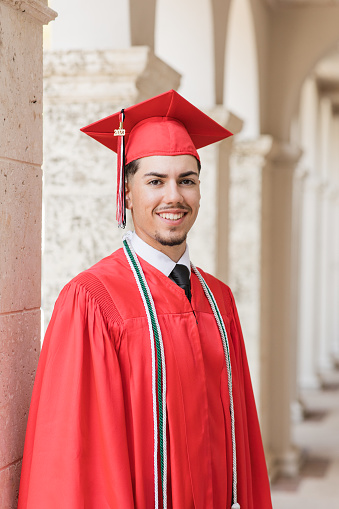 A 2023 High-School Senior Young Man in a Red Graduation Cap & Gown With Three Honors Tassels, A Well-Dressed 18-Year-Old Cuban-American with Brown Hair & Brown Eyes Looking Fresh & Sharp in a Suit & Tie in a Classy Location in Palm Beach, Florida
