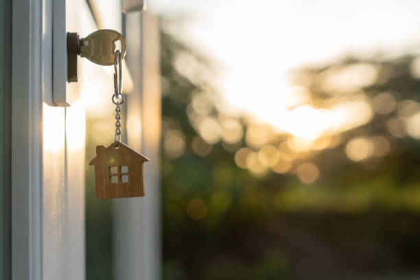 vermieterschlüssel zum entriegeln des hauses ist in die tür gesteckt. gebrauchtes haus zu vermieten und zu verkaufen. schlüsselanhänger weht im wind. hypothek für neues eigenheim, kaufen, verkaufen, renovieren, investition, eigentümer, immobilien - eigenheim stock-fotos und bilder