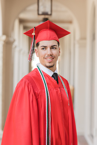 A 2023 High-School Senior Young Man in a Red Graduation Cap & Gown With Three Honors Tassels, A Well-Dressed 18-Year-Old Cuban-American with Brown Hair & Brown Eyes Looking Fresh & Sharp in a Suit & Tie in a Classy Location in Palm Beach, Florida