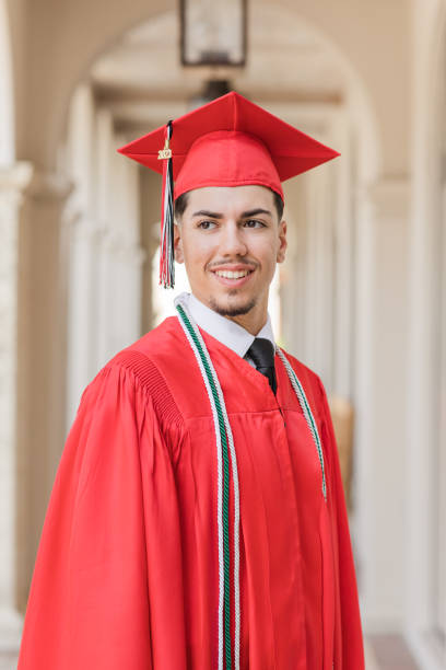 2023 highschool-senior junger mann in einer roten abschlussmütze und einem roten kleid mit drei ehrenquasten, ein gut gekleideter 18-jähriger kubanischer amerikaner mit braunen haaren und braunen augen, der in anzug und krawatte an einem stilvollen ort i - men graduation clothing brown hair stock-fotos und bilder