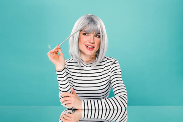 Smiling woman in casual striped shirt looking away Portrait of positive young female in trendy outfit smiling and looking away while sitting against turquoise background gray hair young woman stock pictures, royalty-free photos & images
