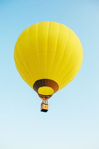 Yellow, red and blue hot air balloon flying overhead in a clear blue sky.