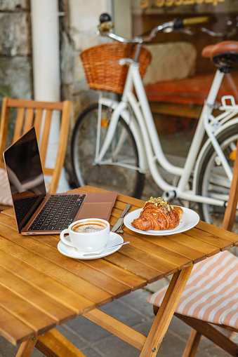 laptop, croissant, and coffee on cafe's summer terrace