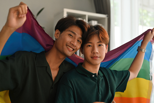 LGBT Asian gay young couple smiling holding pride flag happiness with love together, LGBTQ Lifestyle Pride Month.