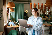 Smiling young woman, girl wearing eyeglasses, freelancer holding laptop and working with happy face in cafe. Social networks, freelance work, business people