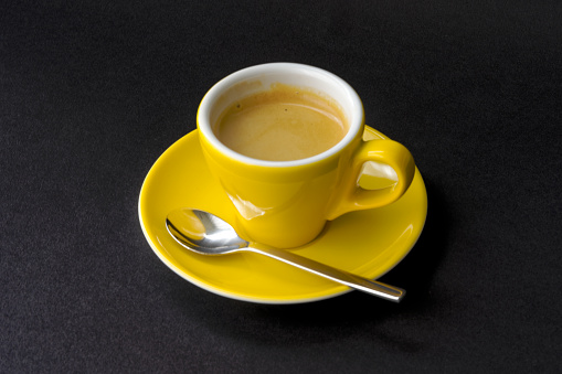 Sun flower yellow espresso cup with saucer and silver colored spoon against black background. Photo taken May 17th, 2023, Zurich, Switzerland.