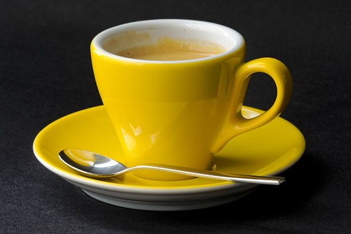 Sun flower yellow espresso cup with saucer and silver colored spoon against black background. Photo taken May 17th, 2023, Zurich, Switzerland.