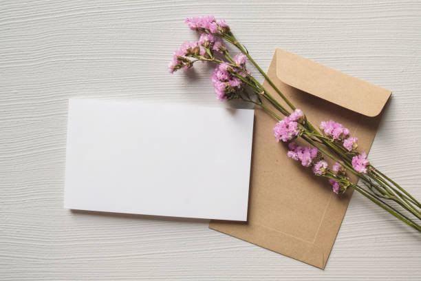 istock White blank greeting or invitation card and envelope with pink flowers decoration on white wooden background. Mock up presentation. 1490983378