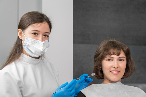 Young smiling woman is sitting in a dental chair, a dentist is sitting next to them, they are looking at the camera. Concept of disease prevention, oral care