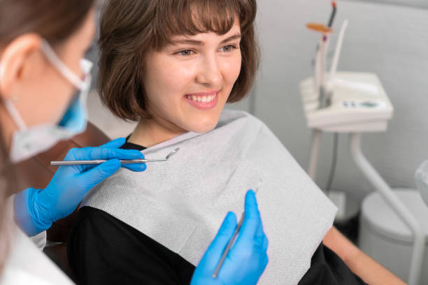 smiling girl in dentist's chair looks at her doctor with confidence, and then turns her gaze directly into camera and smiles, close-up. dental treatment by professional dentist in modern clinic - medical exam dental hygiene caucasian mask imagens e fotografias de stock