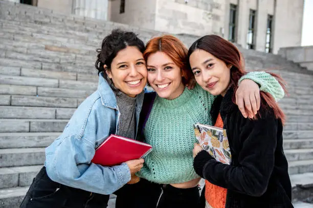 Portrait of young female friends/students embracing each other at street