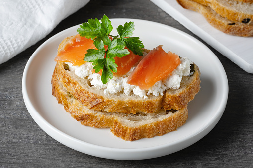 Sandwich with salted salmon and cottage cheese on a gray wooden table.