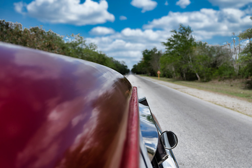 In Holguin Province,  a rural asphalted road with a close-up of  a vintage car,