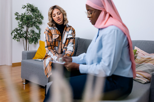 Explore the journey towards holistic well-being as a young Caucasian woman actively collaborates with her psychotherapist, a young Black woman wearing a hijab, working together to address various aspects of her mental and emotional health