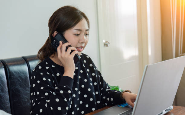 istock Young beautiful woman working and using smartphone with laptop while sitting at desk in home office concept, backlit warm light. 1490988717