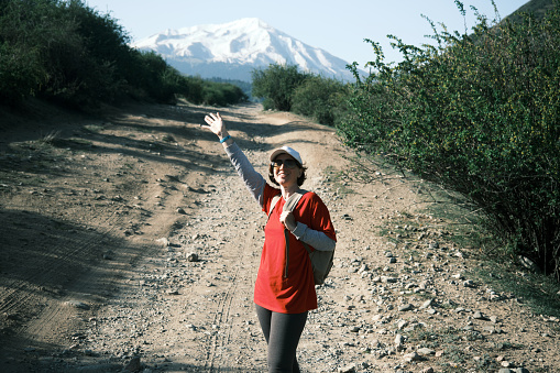 Mature woman is standing on the road and looking around on her way to the mountains in the morning