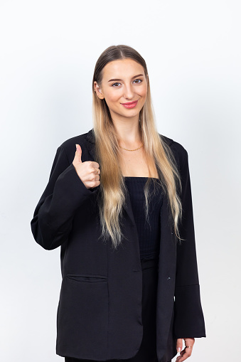 attractive young woman giving  thumbs up gesture and looking at camer. Professional company business woman over white wall background